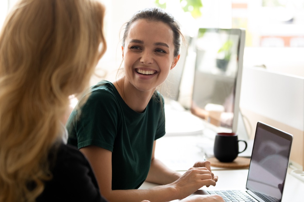 A lady smiling sat at a laptop.