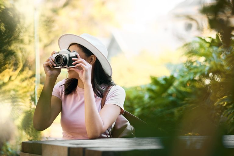 A woman in a garden taking a picture with a camera.